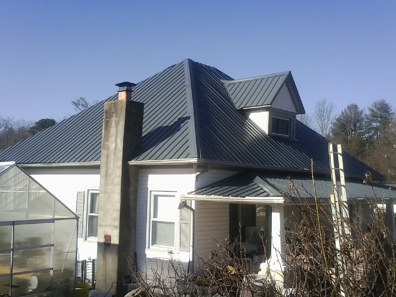 Dark blue standing seam metal roof on a white farmhouse with dormer — Slate & Tile Roof Repair by Roofing Brothers in Gunnison