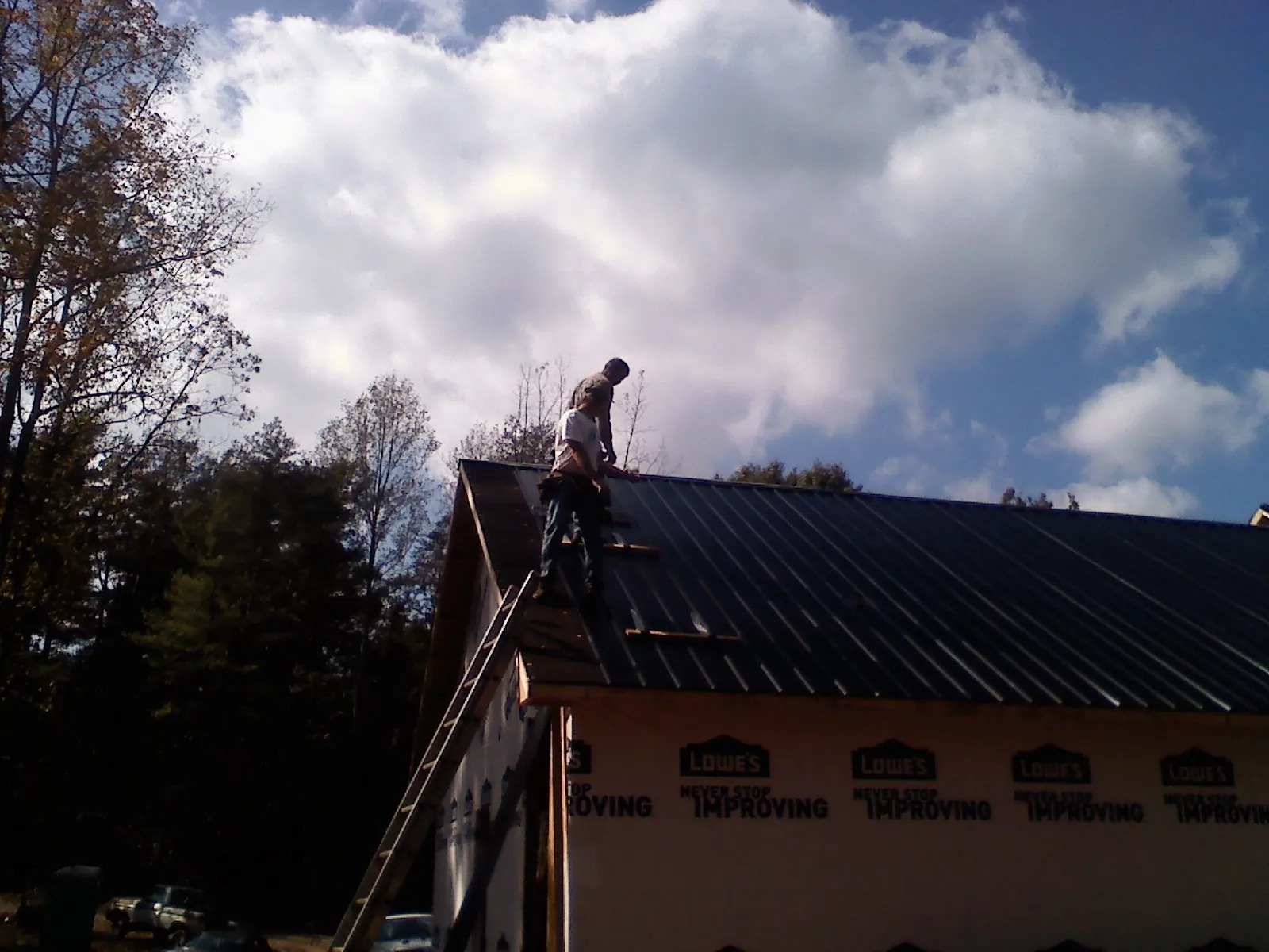 Roofer fastening dark metal panels high against a cloudy sky, from a Roof Inspection job in Gunnison